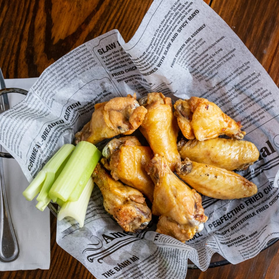 A basket of golden-brown Irish pub chicken wings with celery sticks on newspaper-lined parchment.